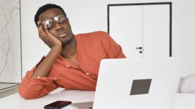 Uykulu Afro-Amerikalı adam masadaki dizüstü bilgisayarın yanında uyanıyor.