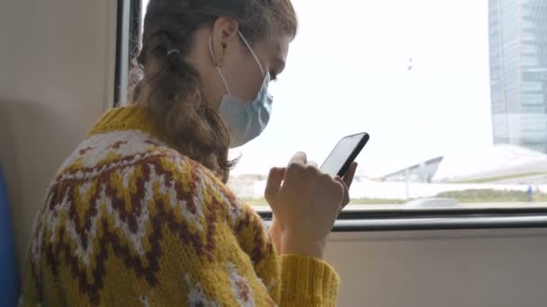 Señora en máscara protectora utiliza el teléfono cerca de la ventana en el transporte — Vídeo de stock