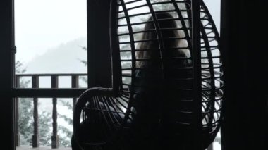 Salıncak sandalyede oturmuş kara bakan bir kadın silueti.