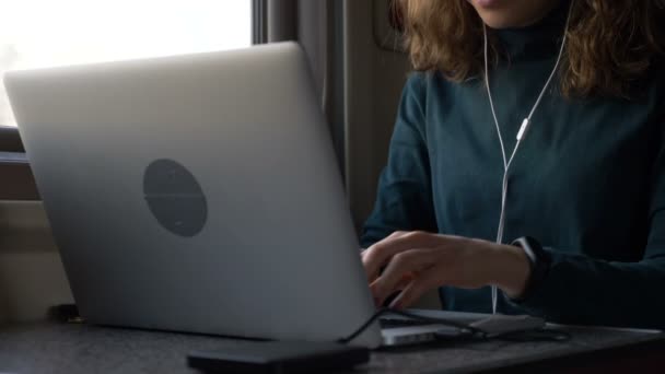 Mladá žena se sluchátky pracuje na notebooku ve vlaku detailní up — Stock video