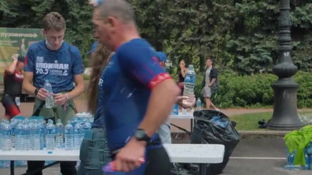 A female volunteer passes a plastic water bottle to an athlete during the Ironman Marathon distance — Stock Video