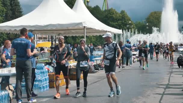 Les athlètes robustes courent le triathlon de momo de fer du point de nourriture et s'arrosent et boivent de l'eau au ralenti — Video