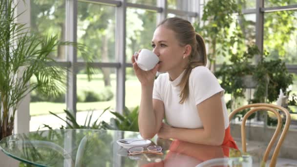 Femme avec des lunettes boit café assis à la table dans le café — Video