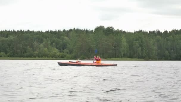 Mother rows kayak with girl sailing along lake near forest — Stock Video