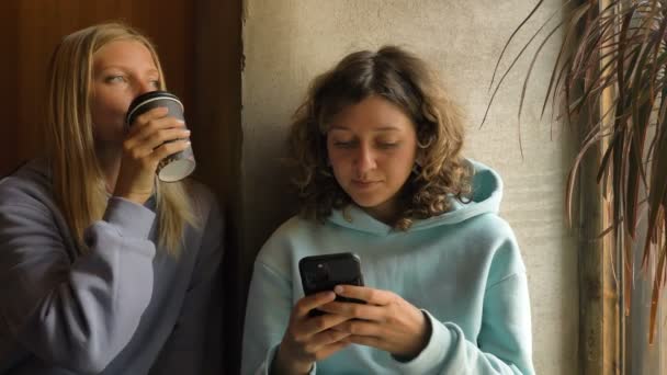 Pozitív nők elegáns kapucnis mobiltelefonok a kávézóban — Stock videók
