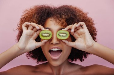 Karışık ırktan genç bir kadın, gözlerinin önünde kivinin yarısını tutuyor.