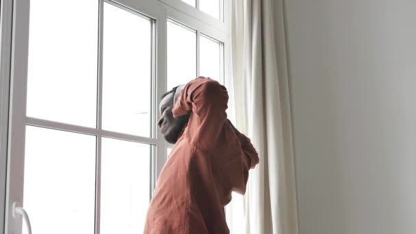 African American man wakes up and stretches standing at the window in the early morning before breakfast and going to work — Stock Video