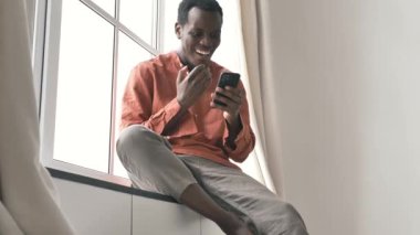 Şaşırmış Afro-Amerikan bir adam akıllı telefondan pervaza bakar.