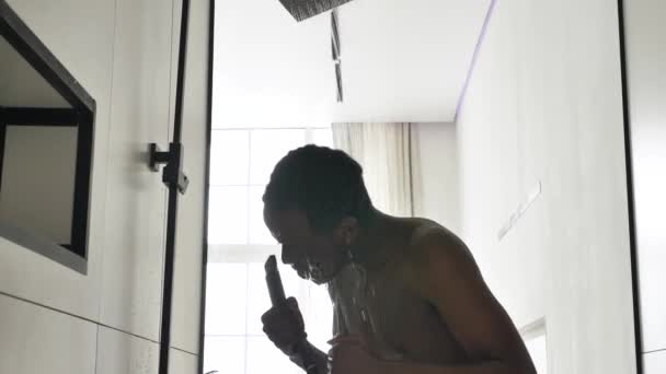 幸せなアフリカ系アメリカ人男性がシャワーを浴びて明るい窓の前で歌を歌う — ストック動画