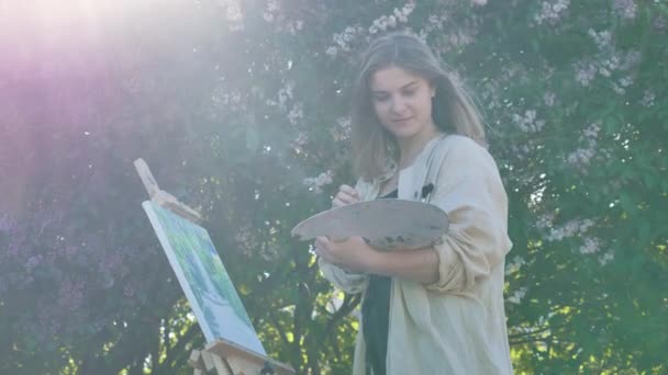 Young woman painter in shirt paints by lilac — Stock Video