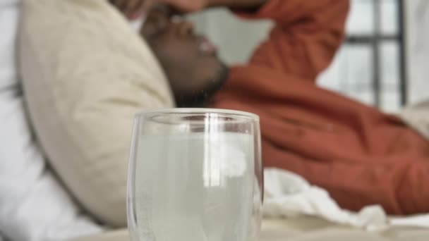 Чёрный афроамериканец лежит в постели с высокой температурой и принимает антипиретики. — стоковое видео