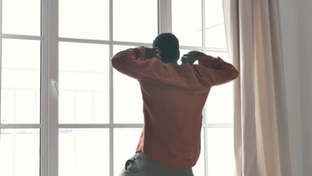 Afroamerykanin rozciąga się przy dużym francuskim oknie — Wideo stockowe