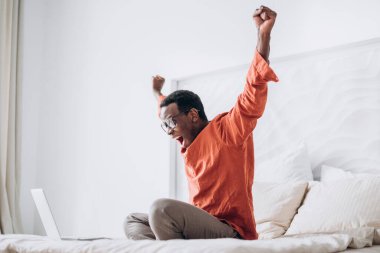 Afro-Amerikalı adam dizüstü bilgisayarın yanında el kaldırıyor.