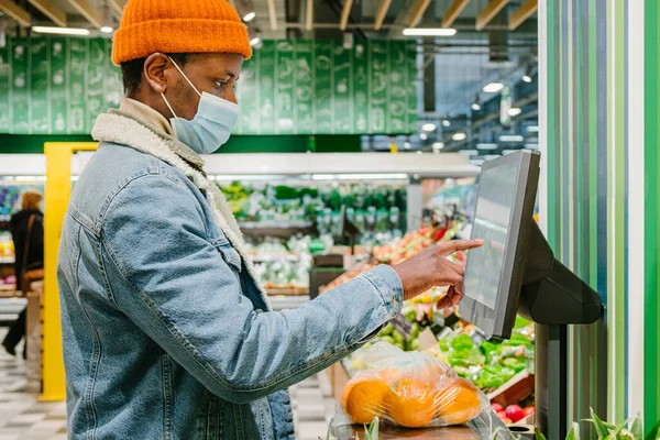 Afroamerykanin w masce waży pomarańcze w supermarkecie — Zdjęcie stockowe