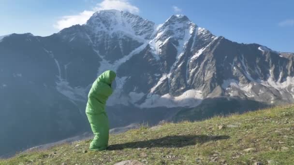 Забавні чоловіки-мандрівники стрибають у спальний мішок на тлі високих засніжених гір у повільному русі — стокове відео