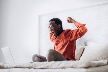 Afro-Amerikalı adam dizüstü bilgisayarın yanında el kaldırıyor.