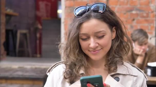 Mensajes de mujer joven en smartphone y bebidas café en la cafetería — Vídeos de Stock