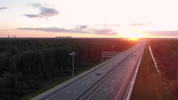Ευρύς δρόμος ανάμεσα στα δάση και την οδήγηση αυτοκινήτων σε πορτοκαλί ηλιοβασίλεμα — Αρχείο Βίντεο