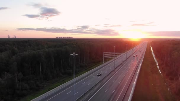 Amplia carretera entre bosques y coches de conducción al atardecer naranja — Vídeos de Stock