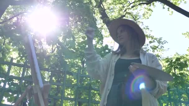 Jovem pintora em chapéu de palha e tintas de camisa por lilás — Vídeo de Stock