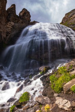 Dağlarda görkemli bir şelale, yüksek bir uçurumdan kayalara düşen bir dağ nehri güneşli bir günde, uzun süre maruz kalan taşlara.
