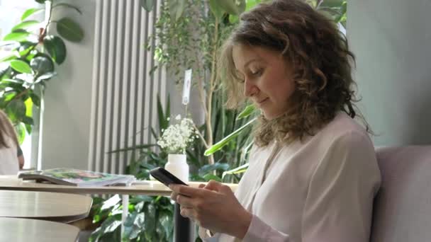 Mujer positiva trabaja en el teléfono en un moderno café verde — Vídeo de stock