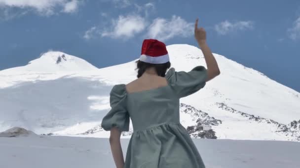 Mulher alegre em um vestido e um chapéu de Natal dança uma dança incendiária contra o pano de fundo do majestoso Monte Elbrus em câmera lenta — Vídeo de Stock