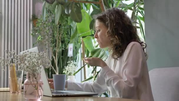 Kobieta z kawą i laptopem bierze kawałek ciasta przy stole — Wideo stockowe