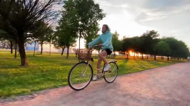 Woman in hoodie and shorts rides bicycle along rural road — Stock Video
