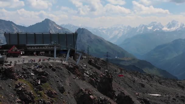 Vista aerea la vecchia cabina rossa ascensore sale alla stazione della funivia negli altopiani sullo sfondo di alte cime di neve — Video Stock