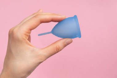 Pembe arka planda mavi regl bardağını tutan bir kadın.