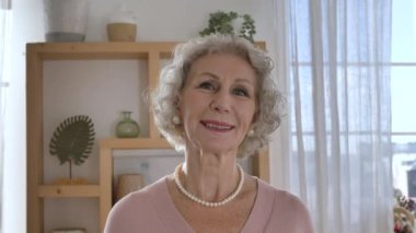 Zarif emekli kadın kameraya bakar ve nazikçe gülümser.