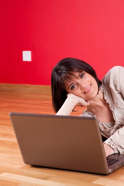 在自家地板上使用笔记本电脑的妇女 在红墙旁边 有选择的焦点 — 图库照片