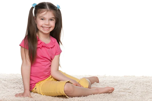Menina feliz senta-se no tapete branco — Fotografia de Stock