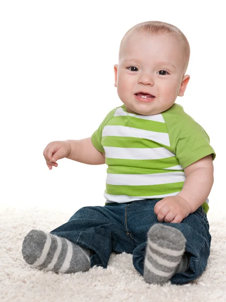 Mosolygós kisfiú ül a fehér szőnyeg — Stock Fotó