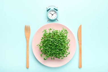 Çalar saat, çatal bıçak takımı ve yeşil tabaklı pembe tabak. Aralıklı oruç, öğle yemeği ve diyet konsepti.