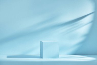 Gölgeli ve ışıklı ürün sunumu için mavi arkaplan. Boş kübik podyum. Model.