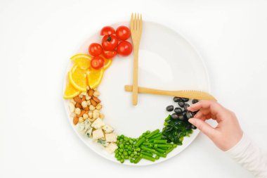 Tabaktaki saat şeklinde dizilmiş renkli yemek ve çatal bıçak takımı. Elde zeytin. Aralıklı oruç, diyet, kilo kaybı, öğle yemeği konsepti.