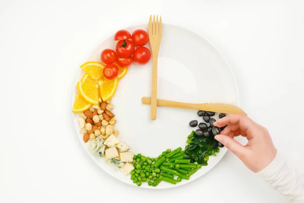 Tabaktaki saat şeklinde dizilmiş renkli yemek ve çatal bıçak takımı. Elde zeytin. Aralıklı oruç, diyet, kilo kaybı, öğle yemeği konsepti.