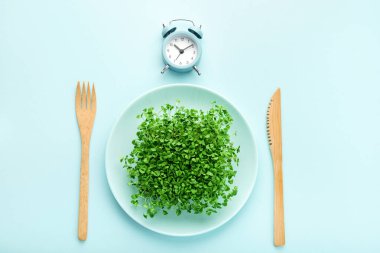 Çalar saat, çatal bıçak takımı ve yeşillikli tabak. Aralıklı oruç, öğle yemeği ve diyet konsepti.