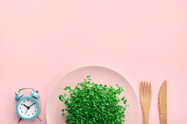 Çalar saat, çatal bıçak takımı ve pembe üzerine yeşillik. Aralıklı oruç ve diyet konsepti.