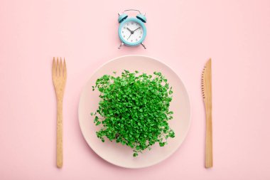 Çalar saat, çatal bıçak takımı ve yeşillikli tabak. Aralıklı oruç, öğle yemeği ve diyet konsepti.