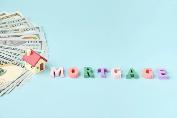 Small house on stacks of money and a word Mortgage. Real estate investment concept, home loan