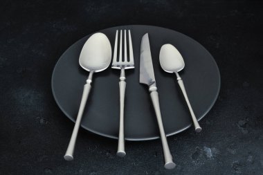 Koyu dokulu arka planda çatal bıçak takımı ve tabak. Tablo ayarı