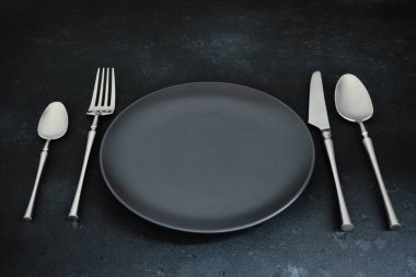 Koyu dokulu arka planda çatal bıçak takımı ve tabak. Tablo ayarı