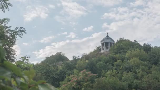 山の上の小さな塔の近くの雲のタイムラプス 緑の木公園 手前の波の葉 — ストック動画