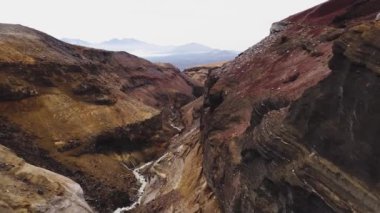 Rusya 'da Kamçatka' da bir dağ kanyonunda uçuyor. Aşağıda kayaların kenarlarında bir dağ nehri görebilirsiniz. Ufukta volkanik bir dağ görünüyor..
