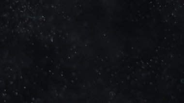 Siyah zemin üzerinde beyaz-gümüş parçacıkların havada asılı kalması. Bazı parçacıklar güzel bir bokeh içinde bulanıklaşıyor. Çeşitli karıştırma kiplerinde videolarınız için 4K arkaplan.