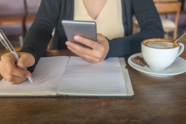 Genç Asyalı bayan akıllı telefon kullanıyor ve notlar yazıyor.