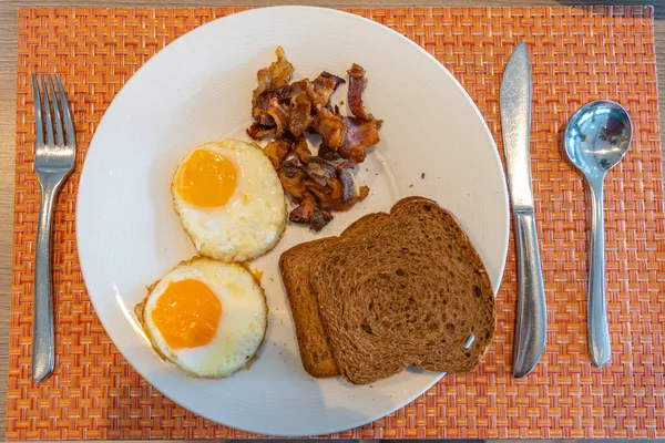 Vue du dessus de l'assiette d'œufs ensoleillés avec pain brun et jambon — Photo